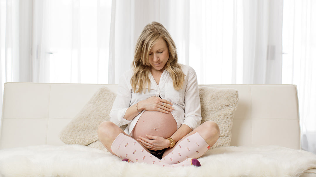 pregnant woman sitting on couch wearing compression socks.