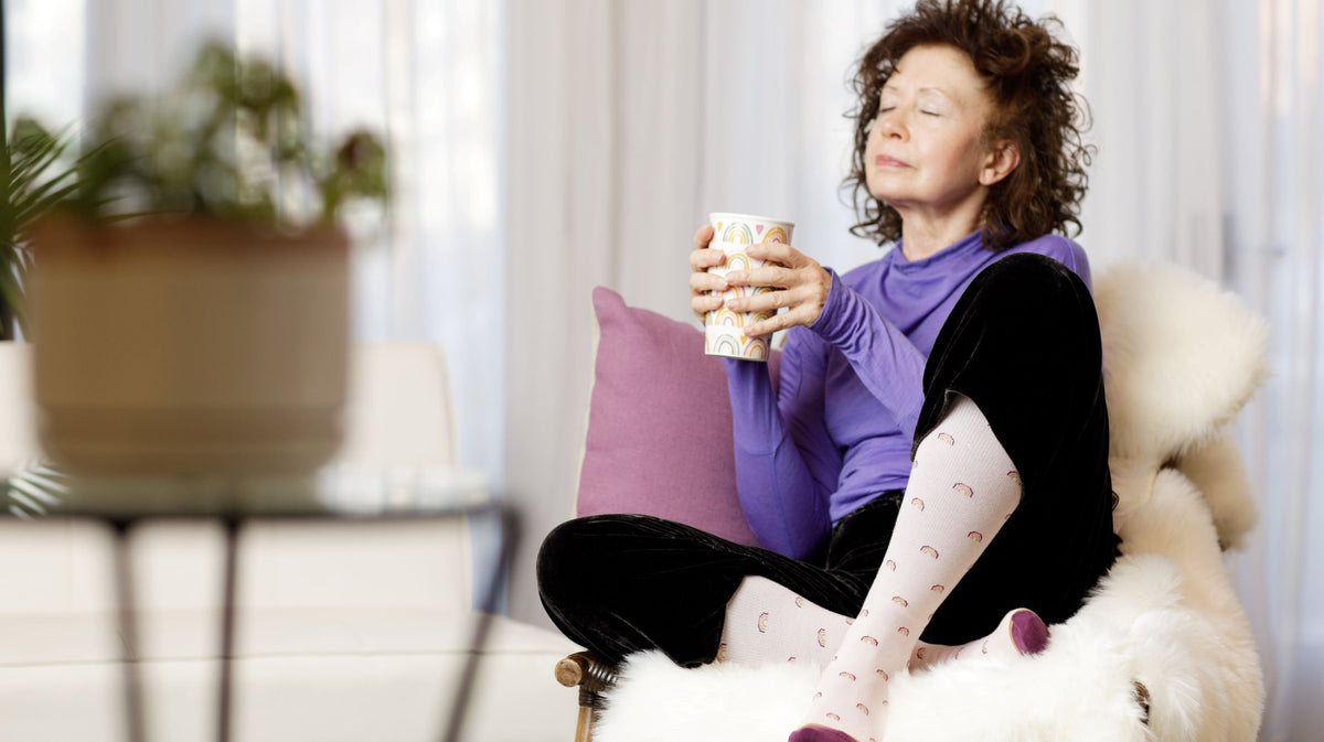 woman sitting on couch while holding a mug and wearing compression socks